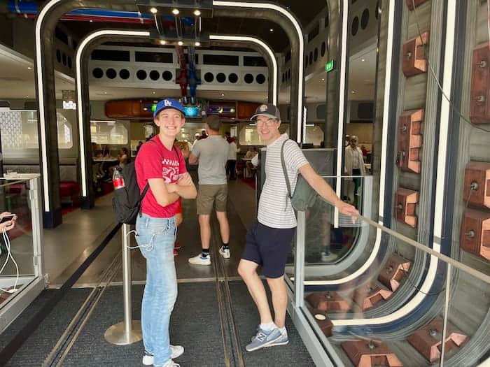 Father and Son in summer clothes queuing outside PYM Kitchen in Walt Disney Studios, one of the best places to be booking restaurants Disneyland Paris