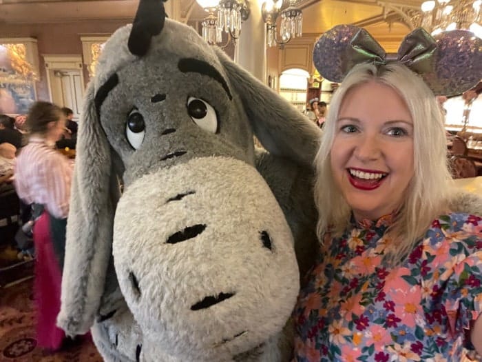 Woman in floral dress and Minnie Ears smiling with Eeyore at the character dining Plaza Gardens