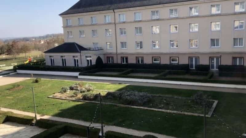 Magic Circus (now Grand Magic) view from upper hotel room. Opposite is white hotel building with a section housing the family pool area. Green grass and a garden area is in the foreground.