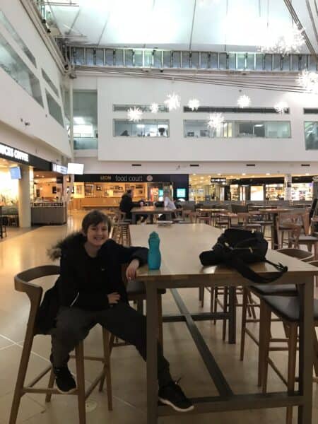 A boy sitting at a tall table in the Eurotunnel Folkestone terminal, surrounded by sparkling fairy lights, on the way to Disneyland Paris by Eurotunnel.