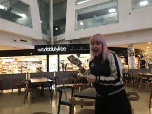 A woman smiling while holding an item at World Duty-Free in the Eurotunnel Folkestone terminal before heading to Disneyland Paris by Eurotunnel.