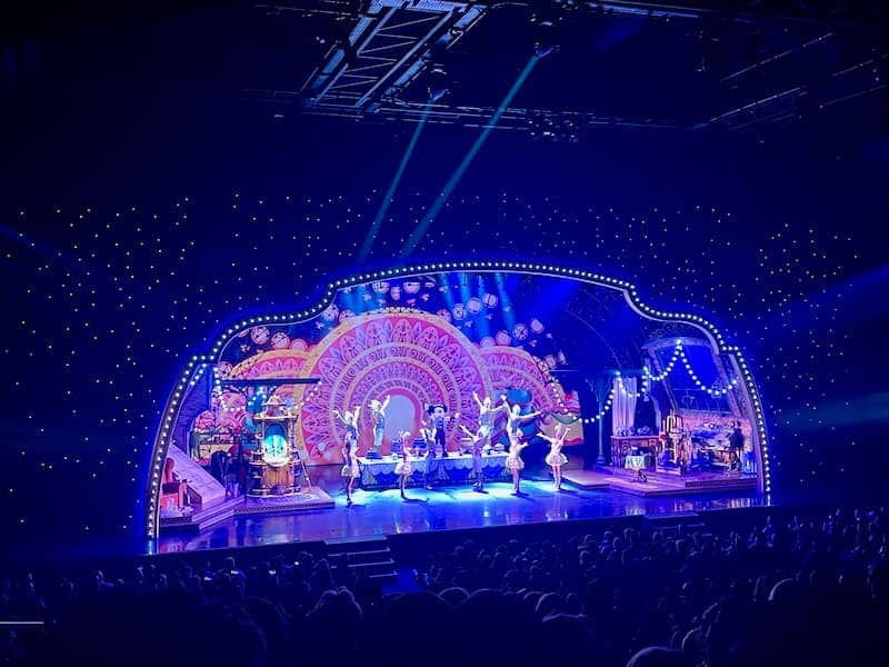 Mickey and the Magician stage show, including Mickey Mouse and characters from popular Disney movies such as Beauty and the Beast. This is the inside of the theatre with the stage lit up in midnight blue. The actors have their hands up, presenting the one and only Mickey Mouse