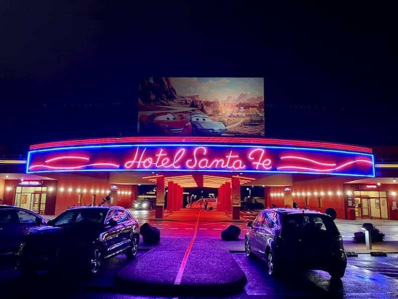 Santa Fe Hotel entrance lit up in neon at night, a poster of Lightning McQueen and Sally hangs above