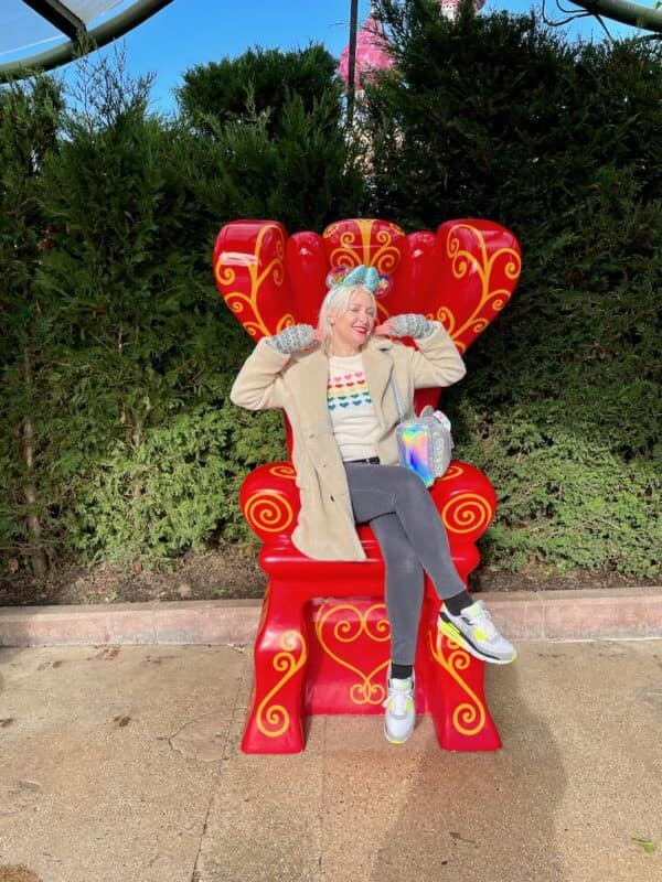 Woman sitting in the Mad Hatter's Chair wearing a colourful sweater, jeans, trainers and warm coat