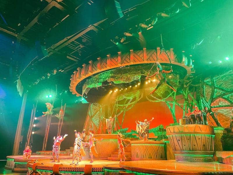 Exuberant performers under green lights perform in African-inspired costumes for Lion King: Rhythm of the Pride Lands - a must do at Disneyland Paris for teenagers