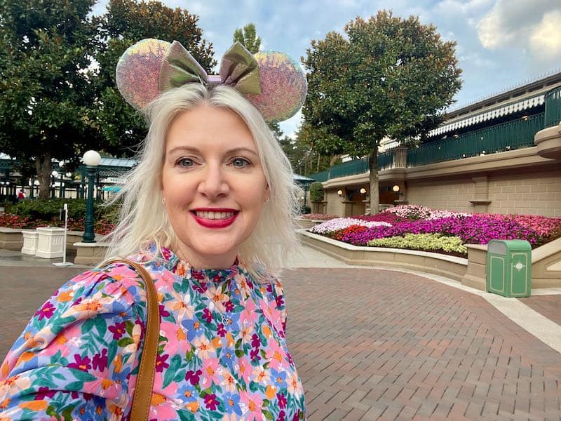 A blonde woman smiling at the entrance to Disneyland Paris
