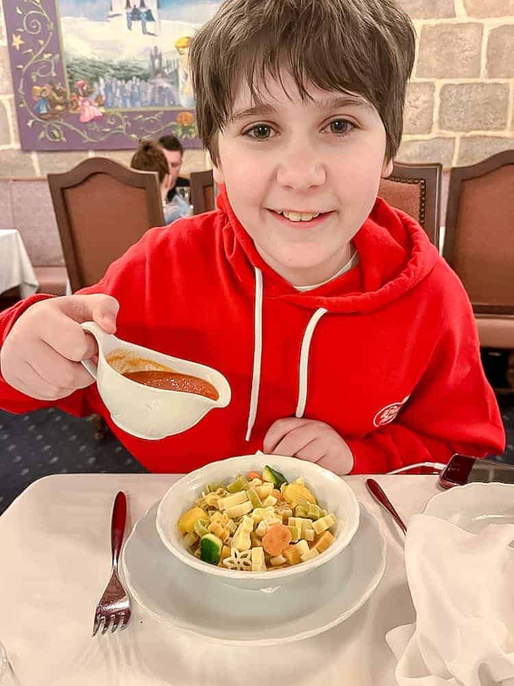 Auberge de Cendrillon princess restaurant offers children's pasta and tomato sauce. A boy in a red top is holding the sauce which comes in a little ceramic gravy dish