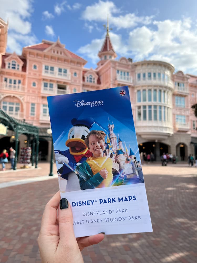 A hand holds up a Disneyland Paris paper map at the entrance to the park