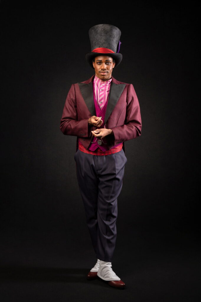 Doctor Facilier greets guests during Halloween at Disneyland Paris 2026, wearing a burgundy tailcoat, purple waistcoat and tall black top hat inspired by Disney's The Princess and the Frog.