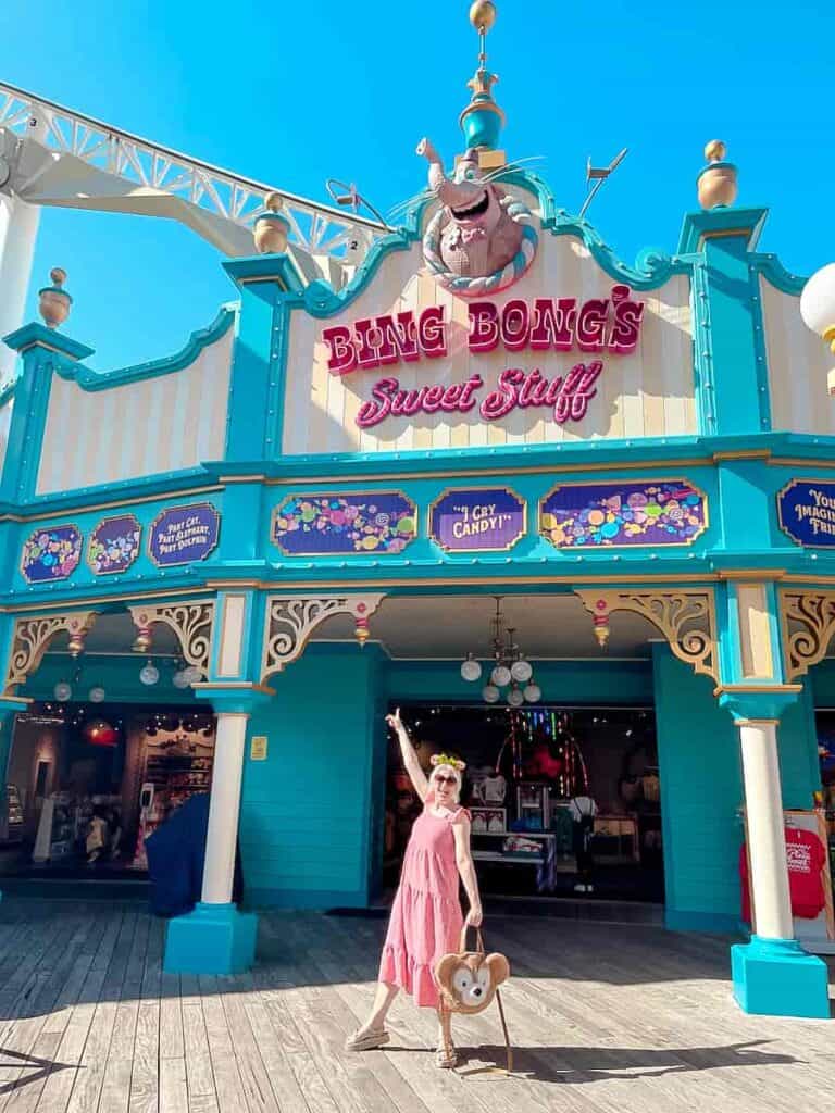 Disneyland Paris blogger Carrie-Anne Hall is in a red summer dress. She is smiling and pointing to a shop called Bing Bong's Sweet Shop in California Adventure, Disney USA