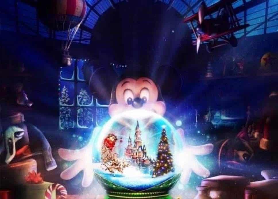 A whimsical Disneyland Paris Christmas 2025 scene featuring Mickey Mouse in a warm, festive setting, holding a glowing snow globe with a miniature Sleeping Beauty Castle inside. The snow globe reflects a twinkling Christmas tree and tiny holiday decorations. The background features a cosy, toy-filled room with soft lighting and a dreamy winter atmosphere, evoking a nostalgic holiday spirit.