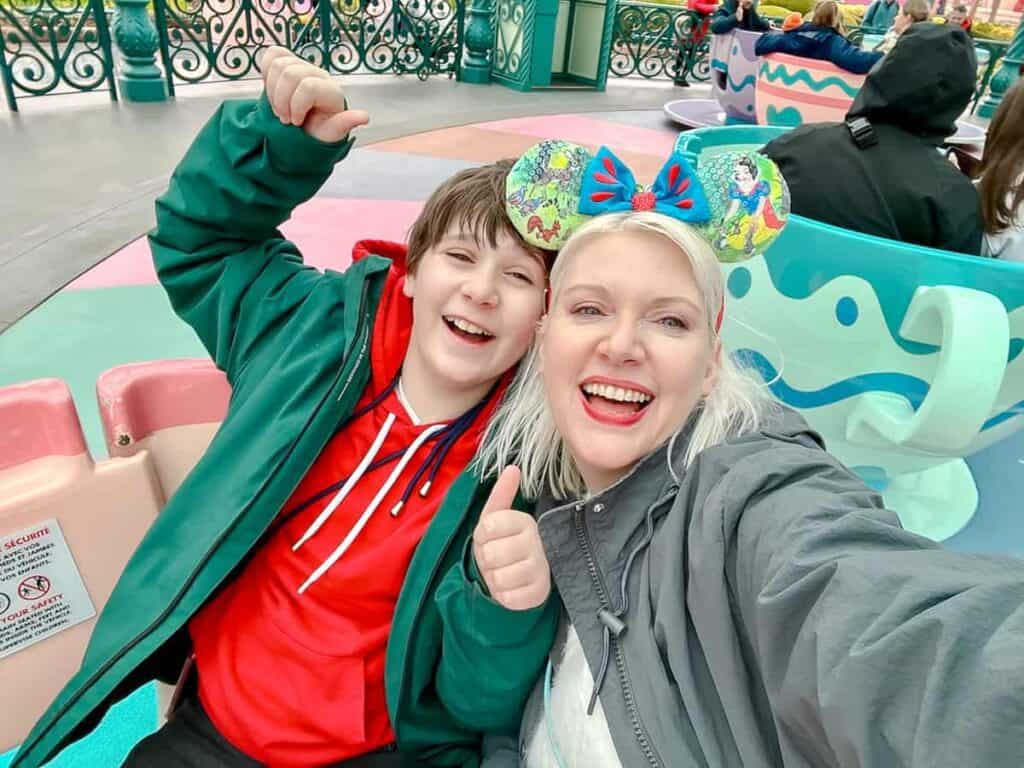 A 13-year-old boy and his mom in the Teacups ride Disneyland Paris, both look excited and are smiling broadly