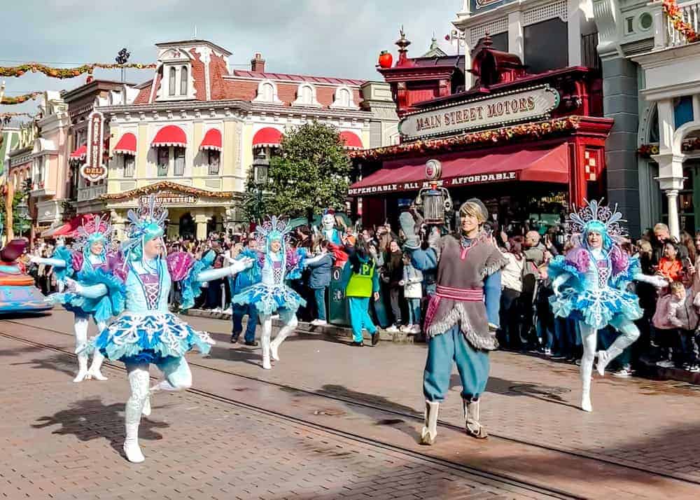 Kristoff from Frozen waves to a guest during Stars on Parade at Disneyland Paris, surrounded by dancers in blue costumes along Main Street U.S.A. — one of the best ways to see Disneyland Paris characters without queueing.