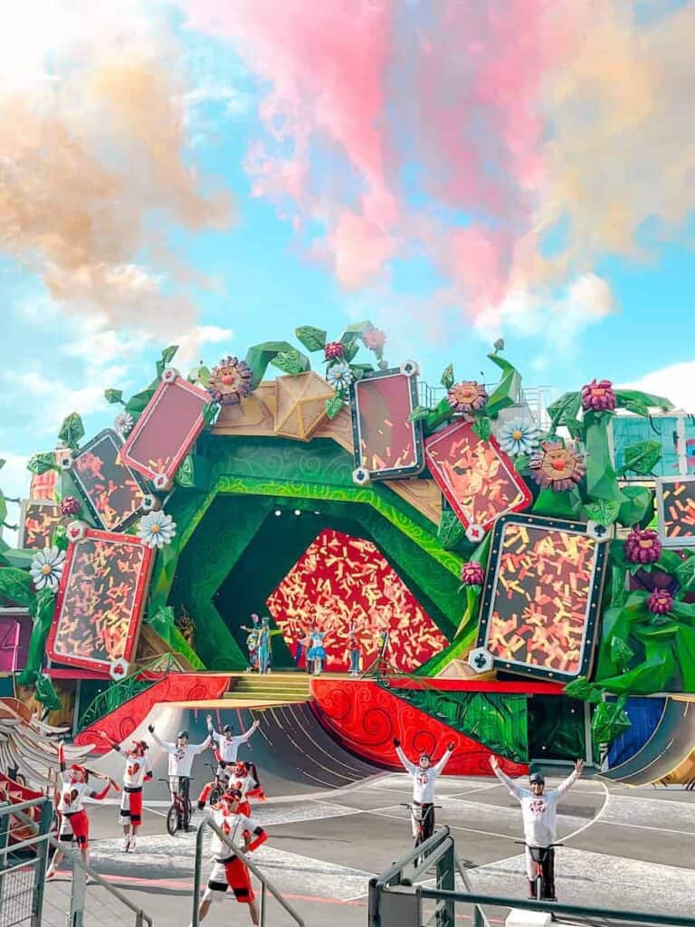 A rainbow of pastel coloured smoke fills the air for the finale of Alice and the Queen of Hearts: Return to Wonderland. In the foreground is BMX bikers, Wonderland characters and trampoline artists holding their hands up to take a bow.