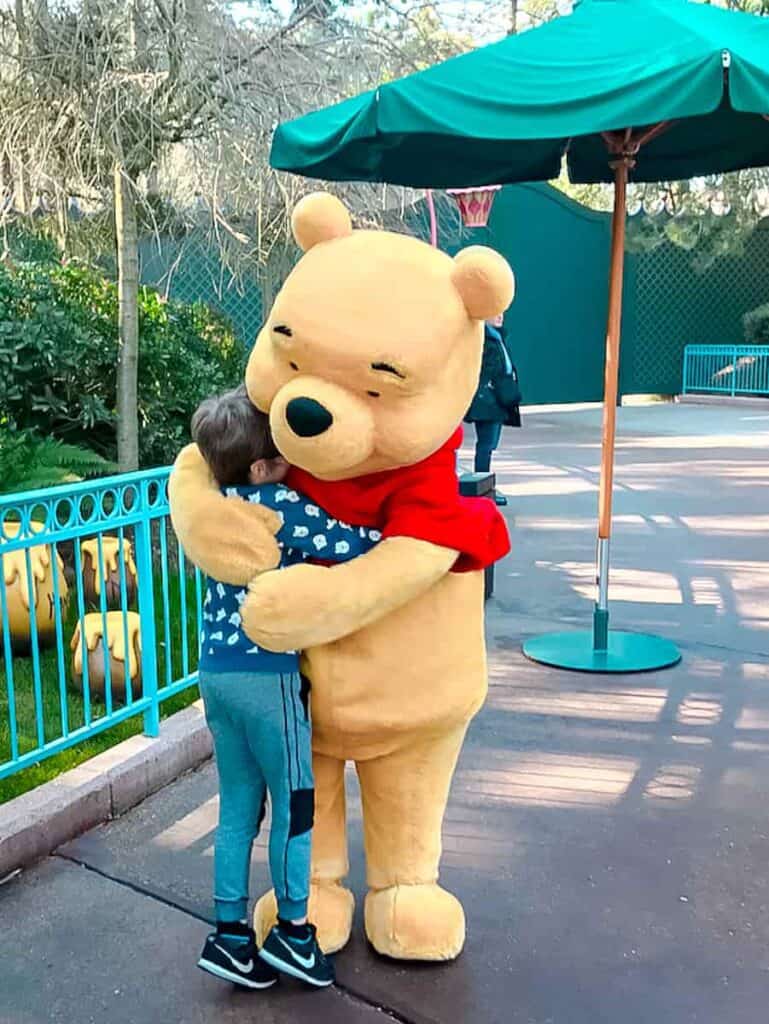 a small boy is swallowed up in a cuddly hug from Winnie the Pooh
