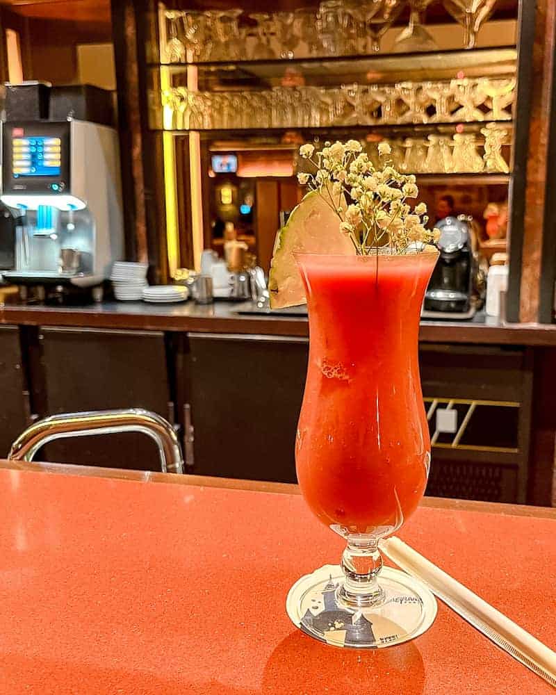 Bright red cocktail garnished with lime and flowers at the stylish bar inside Redwood Lounge, perfect for adults enjoying a relaxed evening at Disneyland Paris.