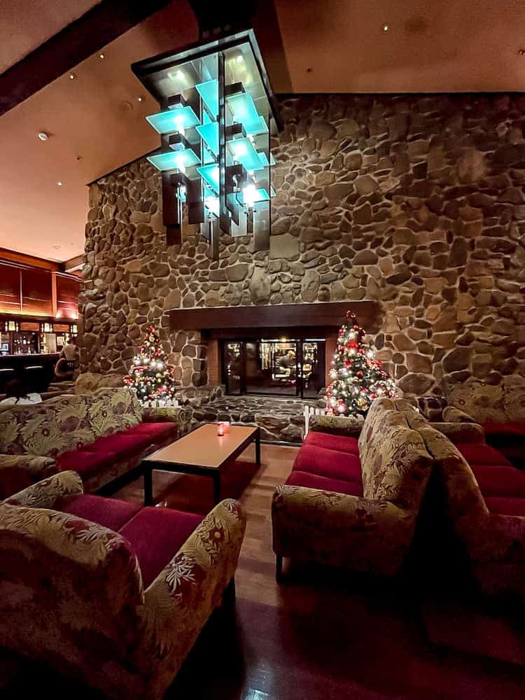 Comfortable adult lounge area at Redwood Lounge, Sequoia Lodge in Disneyland Paris, featuring a roaring fireplace, festive decorations, and plush seating.