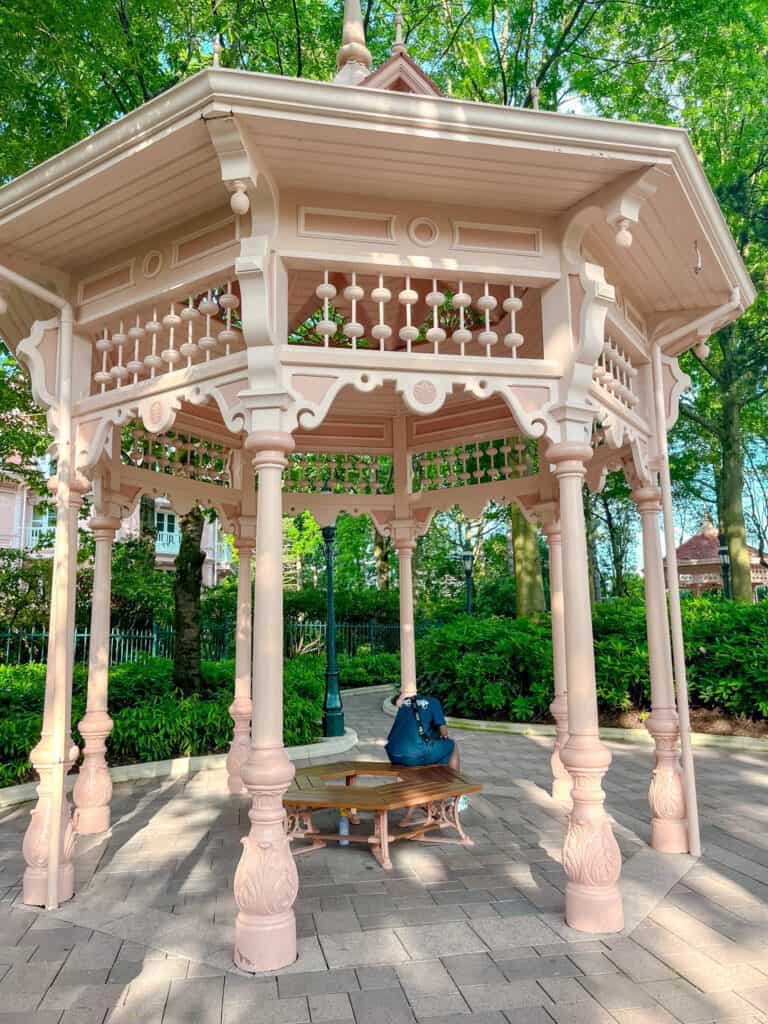 a pretty pink Victorian style gazebo with a person resting on a park bench