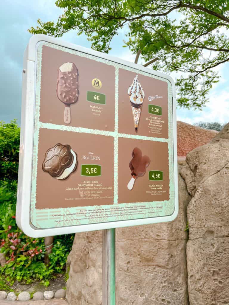 An ice cream menu at a Disneyland Paris snack kiosk shows Magnum, Cornetto, Lion King Paw Print Sandwich and Mickey ice cream bar at affordable prices