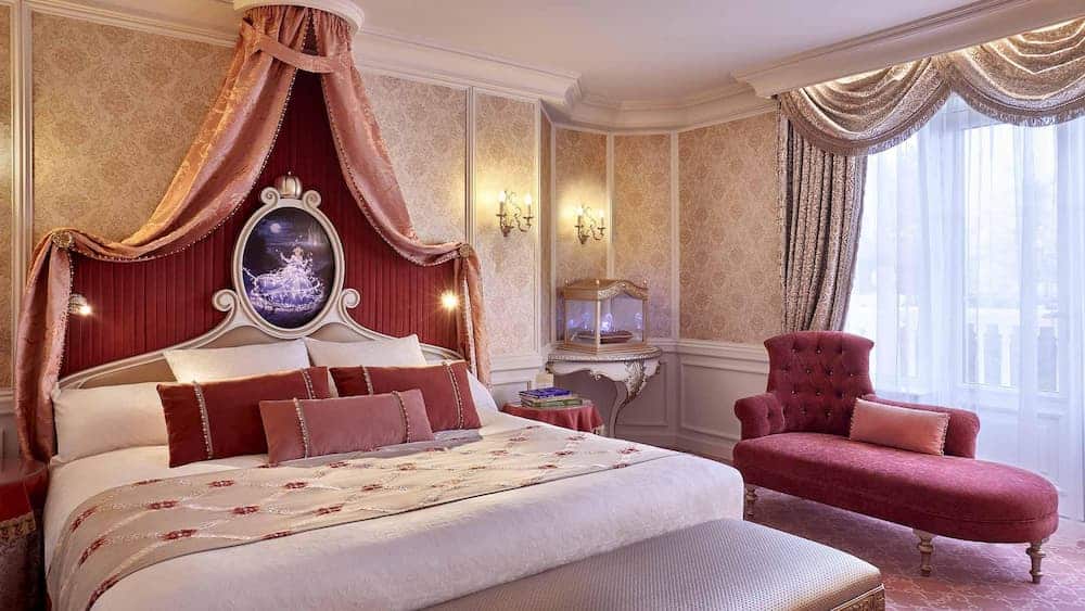 Elegant Cinderella-themed bedroom at the Disneyland Hotel in Paris, featuring a canopied bed, royal décor, and a framed scene from the fairytale above the headboard.