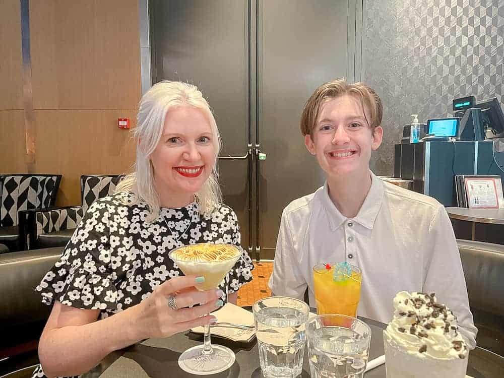A blonde woman and her teenage son have colourful cocktail drinks at the Skyline Bar Art of Marvel Hotel