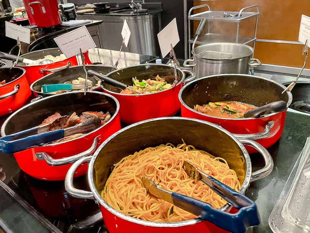Several large red pots holding delicious food like pasta, noodles and sauces