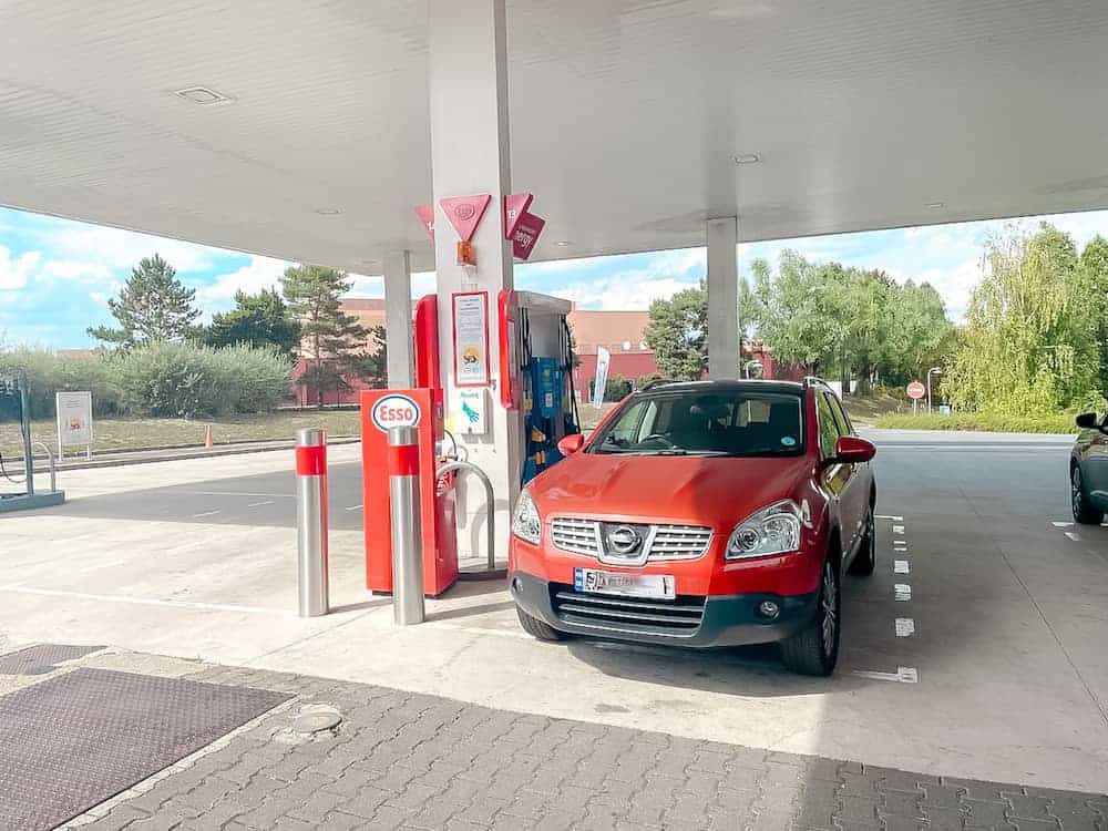 A red car parked at an Esso petrol station in France, refuelling during a road trip.