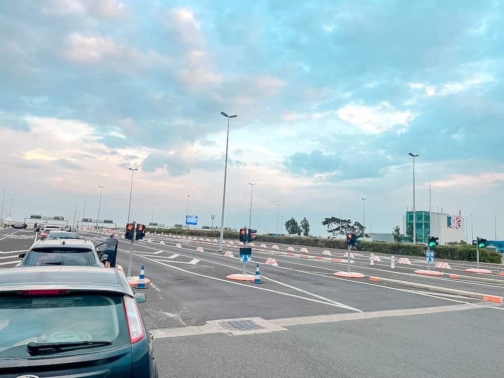 Cars lined up at a Eurotunnel check-in point in Calais, France, with a clear sky in the background.