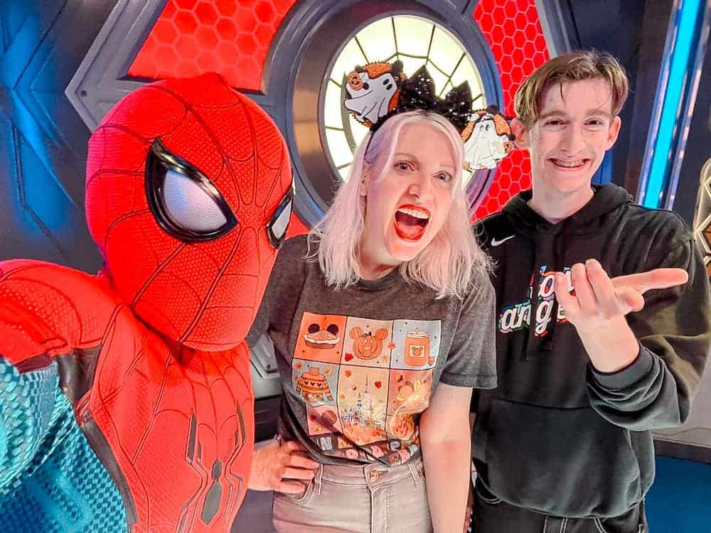 Spider-Man, a blonde woman with a Halloween headband, and a teenage boy are posing for a selfie