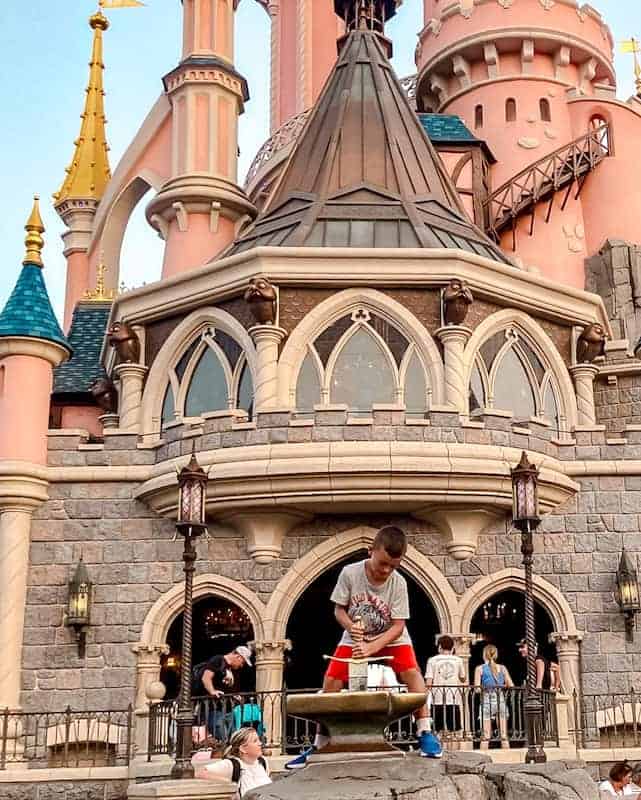 A younger child aged 5 is trying to pull a sword from the stone in the back of Sleeping Beauty Castle