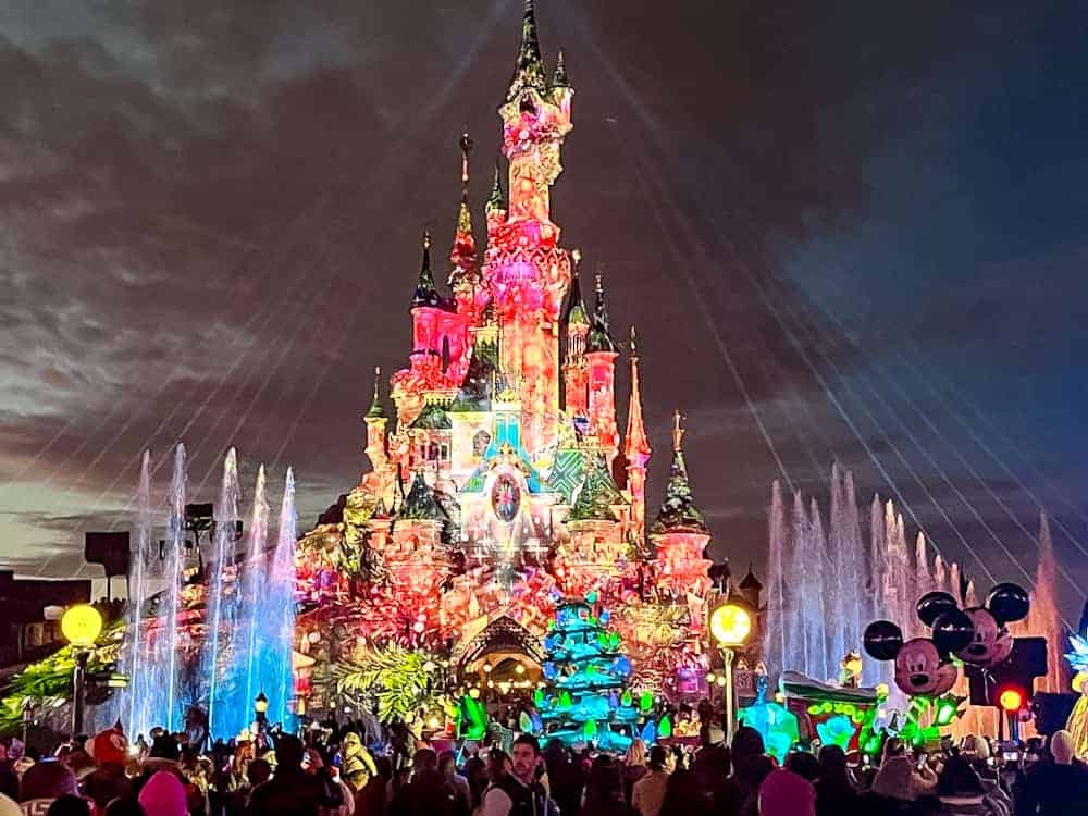 Standing in the crowd at Disneyland Paris with the Sleeping Beauty Castle glowing in the background, an ideal spot for Mickey’s Dazzling Christmas Parade tips and tricks.