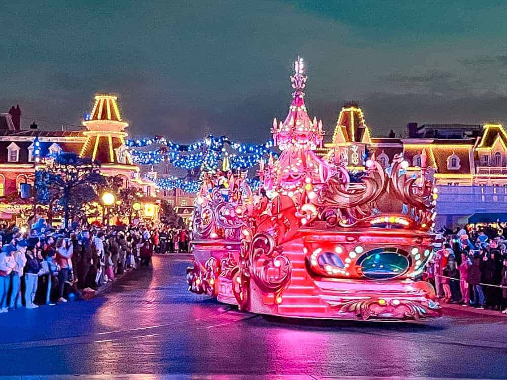 An ornate float adorned with festive lights and holiday decor shines brightly as it moves down Main Street during Mickey’s Dazzling Christmas Parade. The Disability Access area is seen on the right.