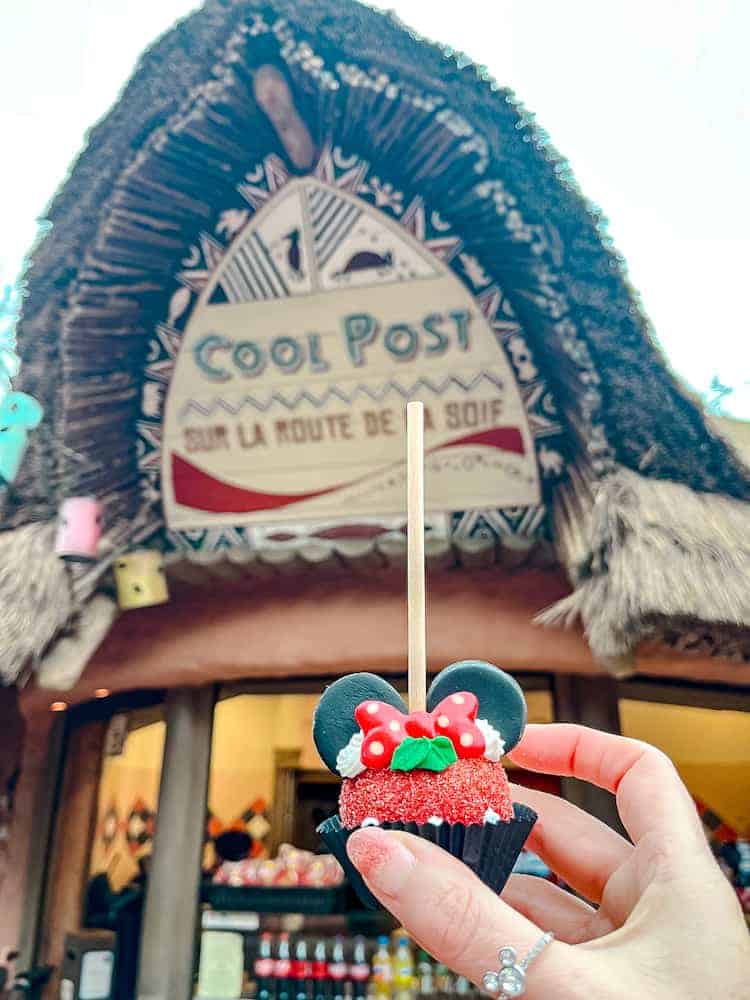 A Minnie Mouse-themed cake pop with festive decorations held in front of the Cool Post at Disneyland Paris, part of the festive treats mentioned in my Disneyland Paris Christmas review.