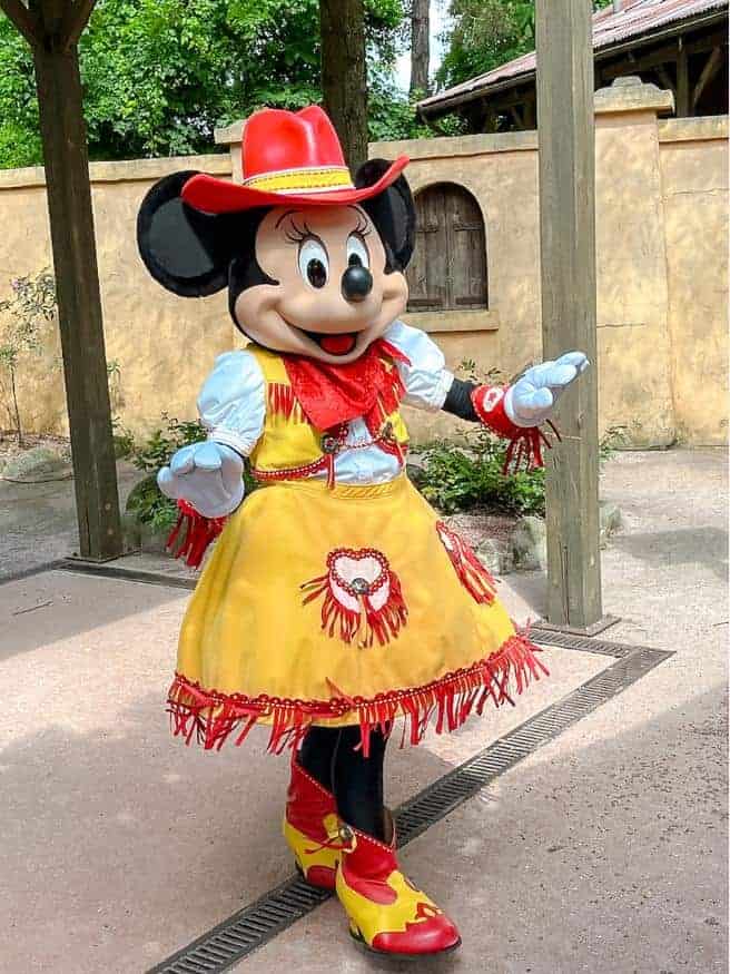 Minnie Mouse is meeting guests at Disneyland Paris in a yellow and red western-inspired dress, cowboy hat and boots