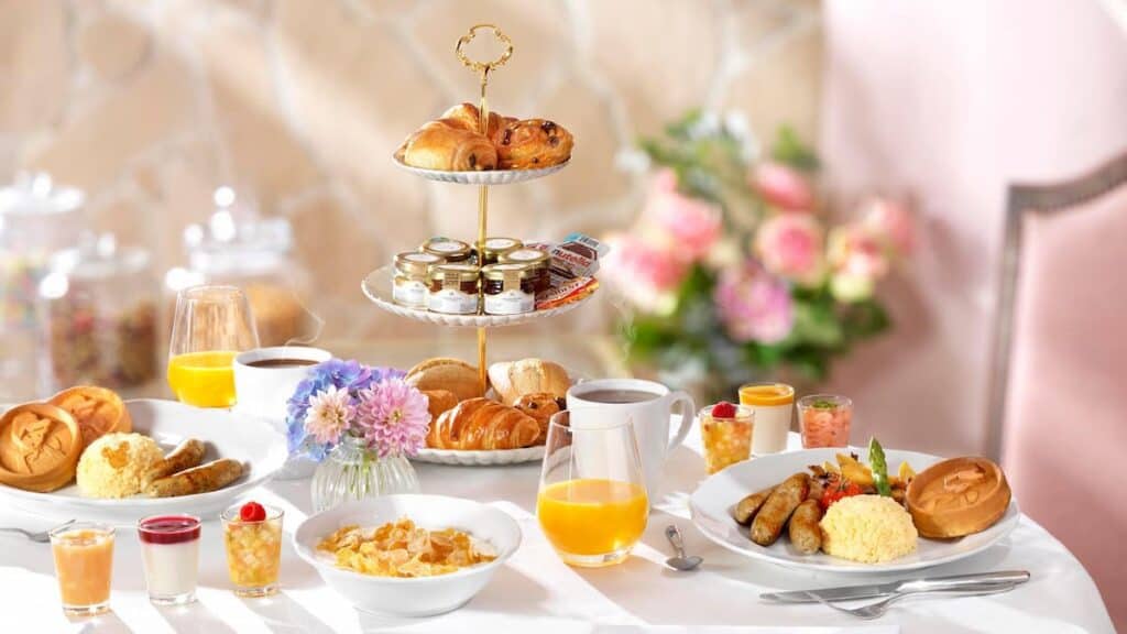 An elegant table set with the Auberge de Cendrillon breakfast menu. Pastries, jams, juices, and hot breakfast dishes are presented; perfect for a royal start to the day.