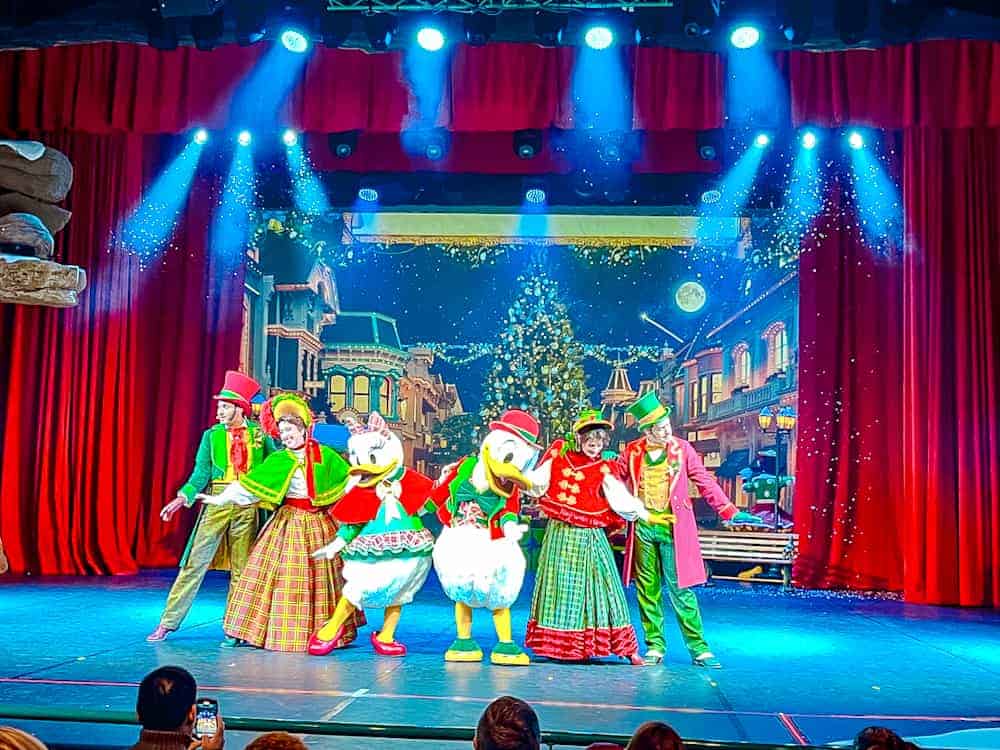 Mickey, Minnie, Donald, and friends performing in festive costumes during a holiday-themed stage show at Disneyland Paris in winter.