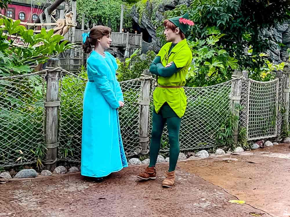 Peter Pan and Wendy sharing a whimsical moment in a lush garden setting during a winter day at Disneyland Paris.