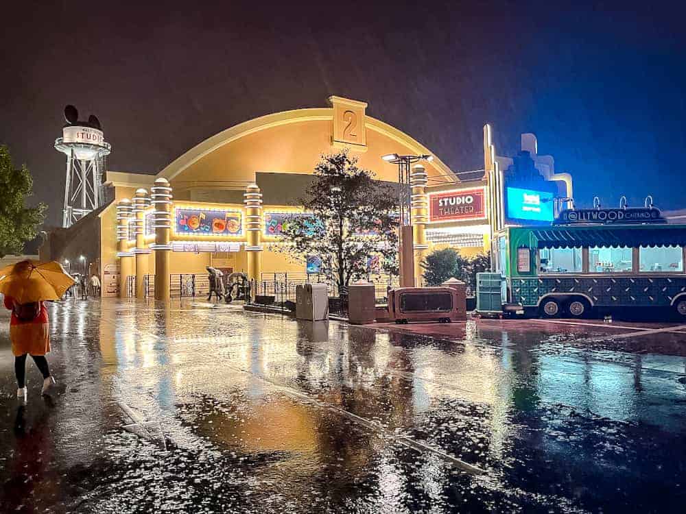 A rainy night scene outside Walt Disney Studios, with glowing lights reflecting off the wet ground, showcasing the charm of Disneyland Paris in winter.