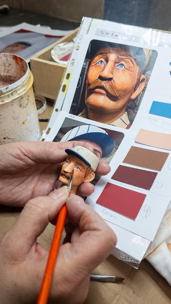 A close-up of a hand painting the detailed face of a Disneyland Paris popcorn doll, showcasing the artistry behind these park treasures.