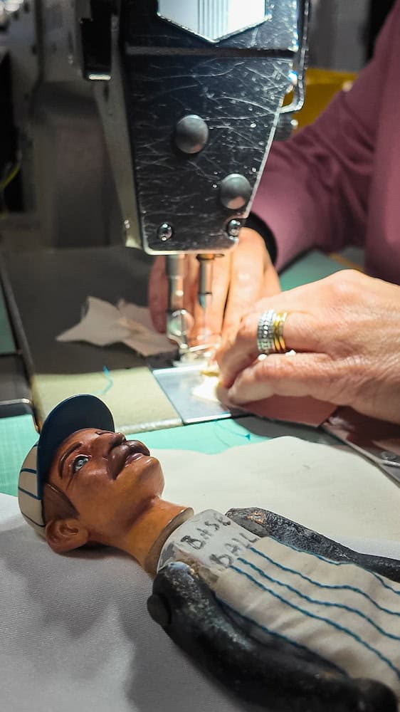 A seamstress works on a miniature costume for a Disneyland Paris popcorn doll, highlighting the care taken to match each doll to its themed land.