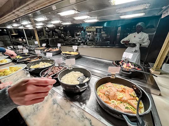 Variety of hot dishes at Plaza Gardens Disneyland Paris buffet, including salmon, rice, and meat options