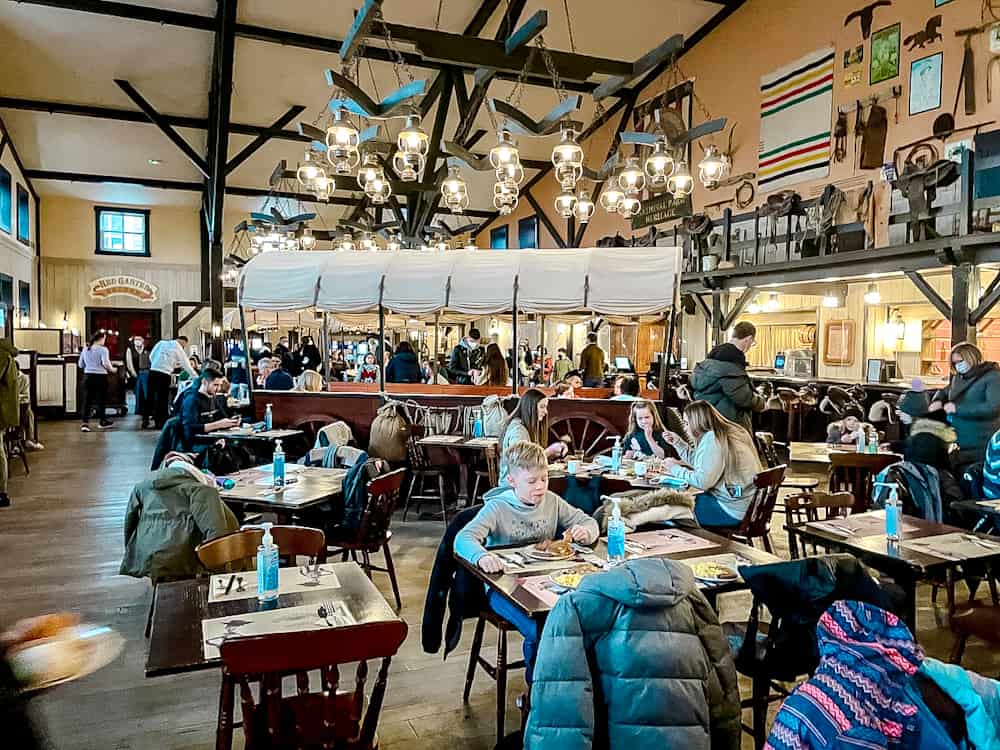 A busy breakfast dining area at Hotel Cheyenne Disneyland Paris, featuring rustic decor, wooden tables, and a warm atmosphere at one of the Disneyland Paris breakfast buffets.