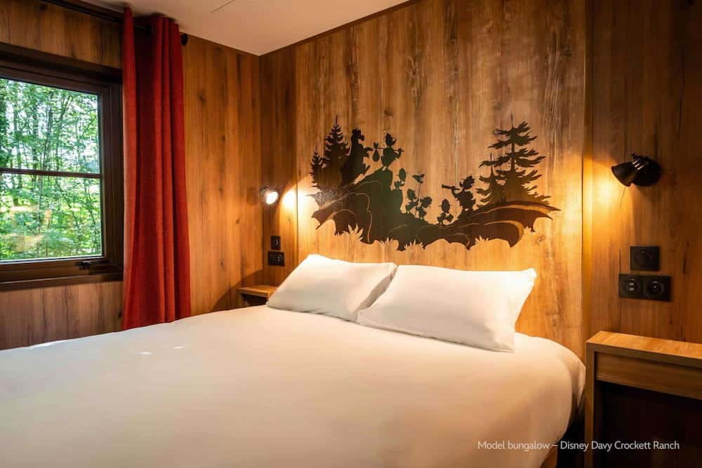 A cosy double bedroom at Disney Davy Crockett Ranch featuring warm wood-panelled walls and a forest-themed silhouette of the Junior Woodchucks above the bed.