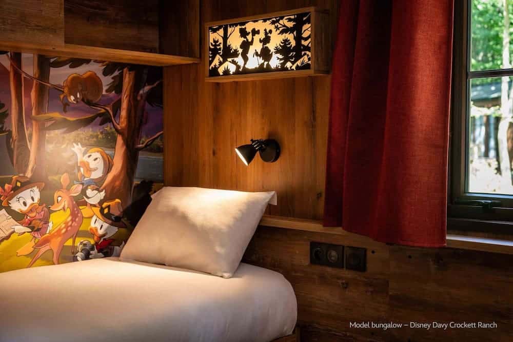 A single bed next to a colourful mural of Huey, Dewey, and Louie exploring the forest with woodland creatures, part of the new Junior Woodchuck theming at Disney Davy Crockett Ranch.