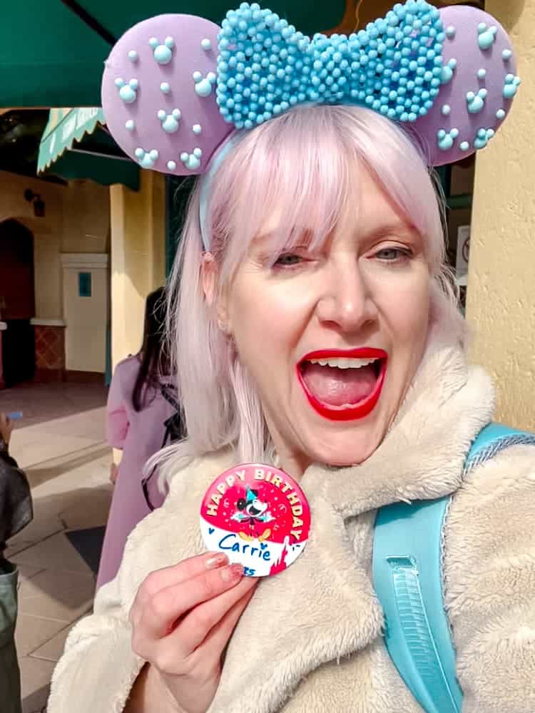 Blogger Carrie-Anne wearing her Disneyland Paris birthday badge with pink Minnie ears and a big birthday smile