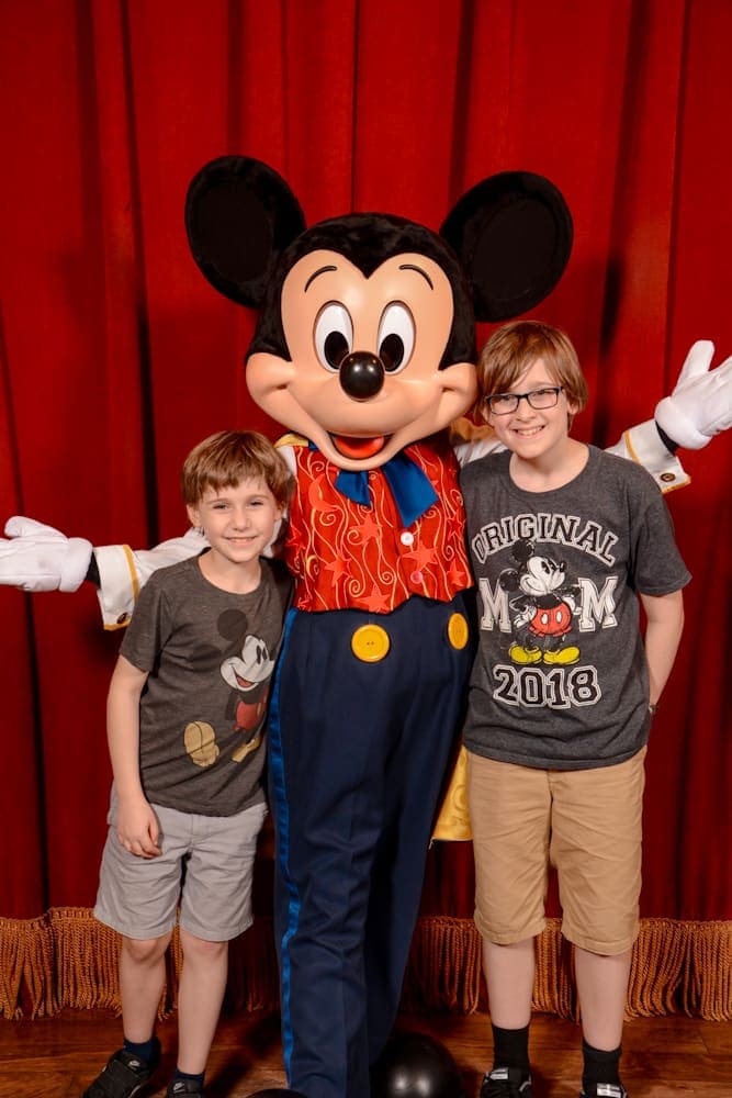 Two children posing with Mickey Mouse at Meet Mickey in Fantasyland, which now uses the Disneyland Paris Virtual Queue system.