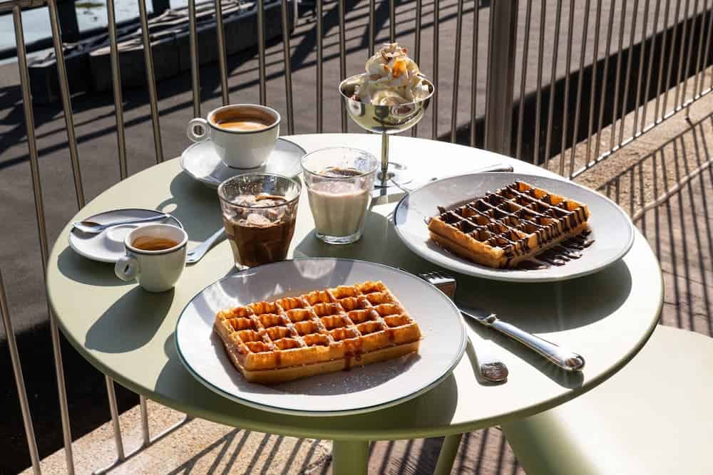Sweet waffles with chocolate drizzle and espresso drinks on a table at Petite Rosalie Terrace in Disneyland Paris