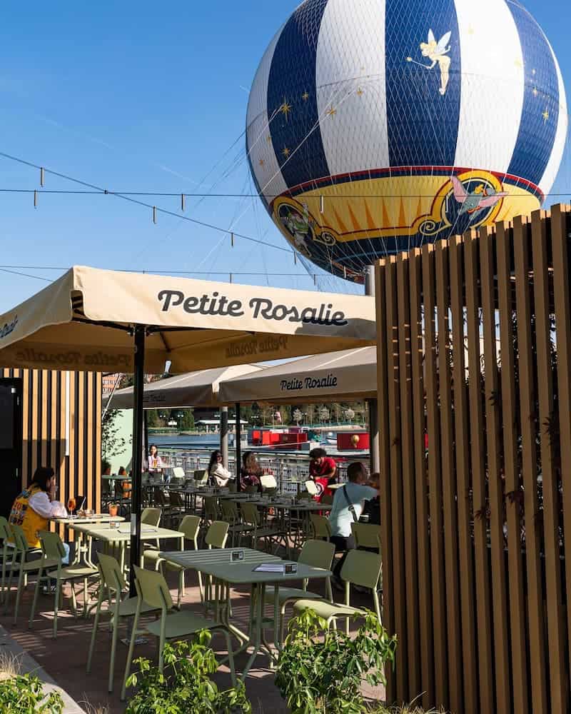 The Petite Rosalie Terrace at Disneyland Paris, showing shaded tables and views of the PanoraMagique balloon by Lake Disney