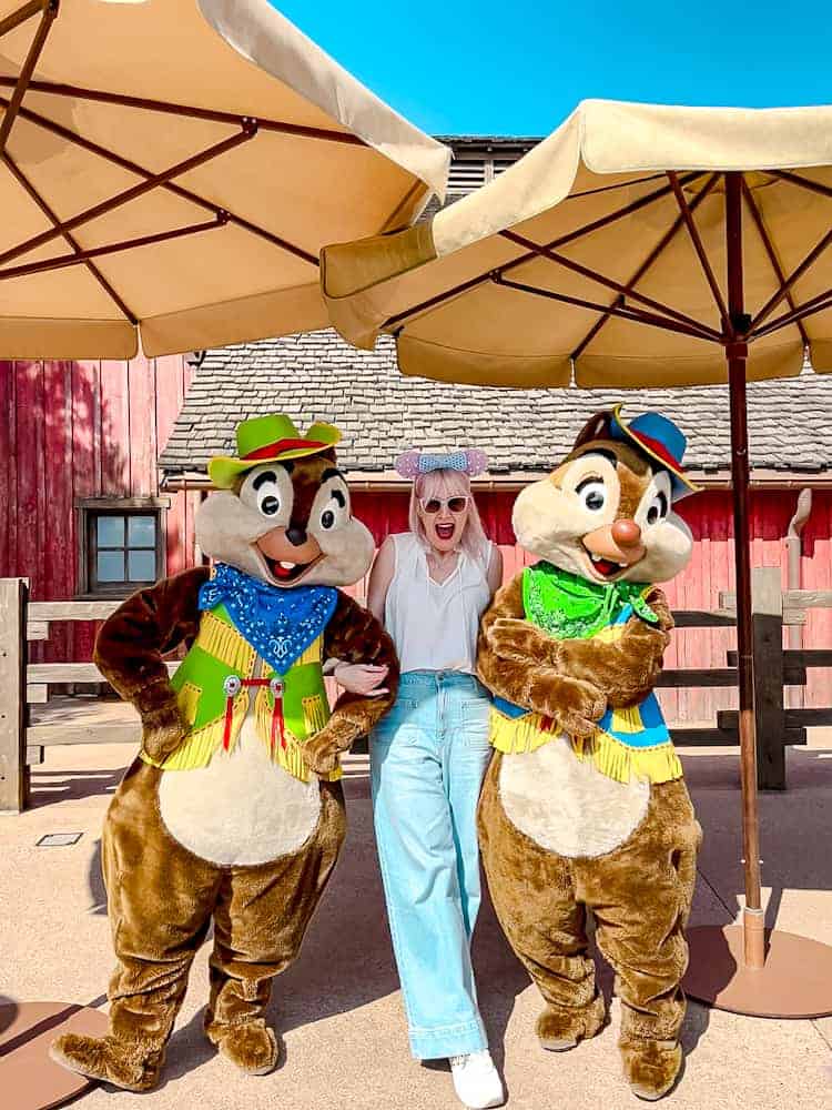 Blogger Carrie-Anne poses with Chip and Dale in their spring outfits under a sunny blue sky in May Disneyland Paris