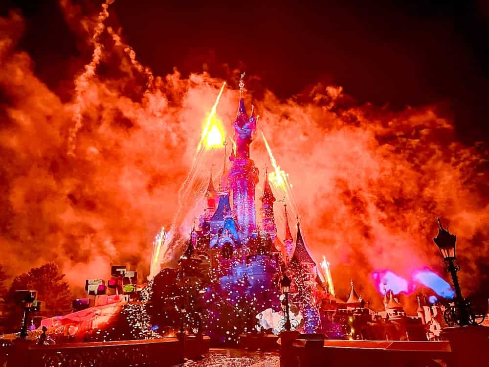 Disneyland Paris castle glowing under a fiery May night sky during the fireworks spectacular.